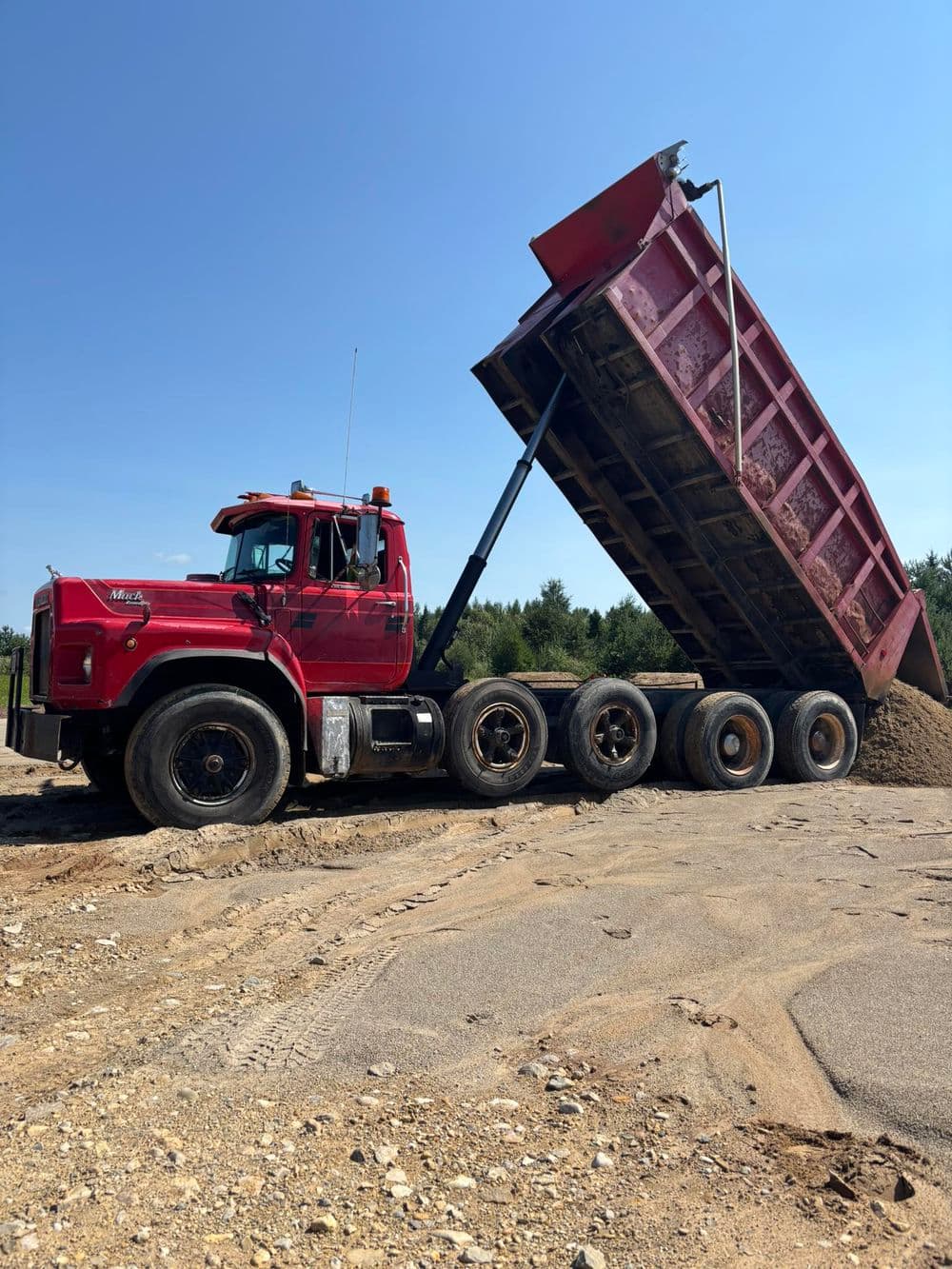 Red dump truck unloading sand at a construction site under a clear blue sky.