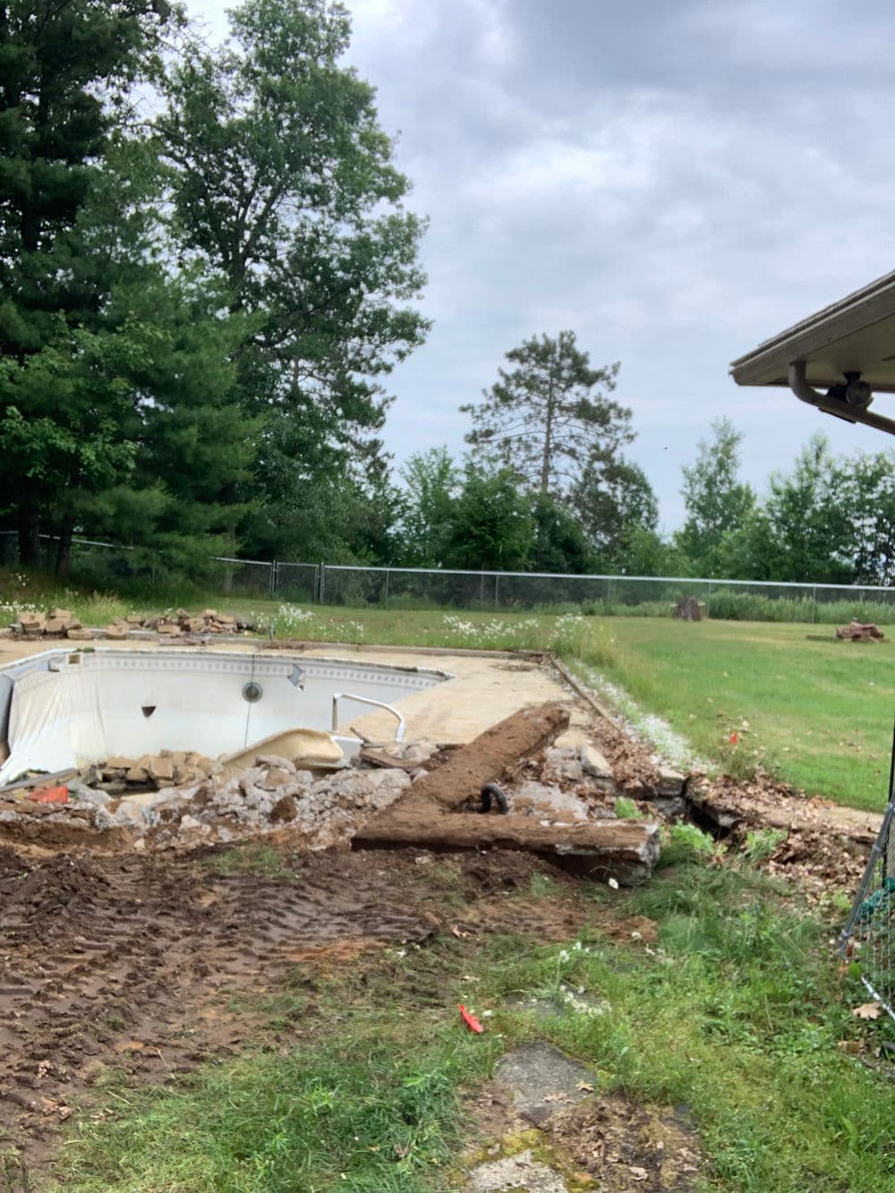 Residential pool renovation with construction debris and overcast sky in a green backyard.