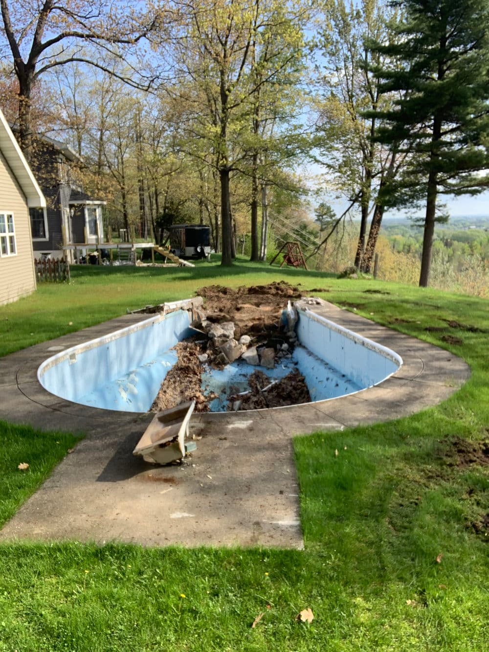 Empty, under-construction swimming pool surrounded by trees and grass in a backyard.