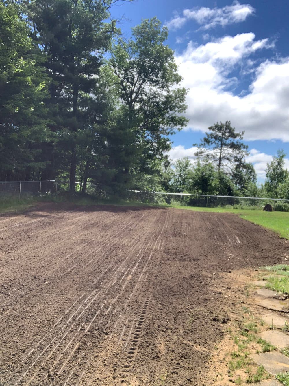 Cleared garden plot under a blue sky, surrounded by trees and nature. Ideal for planting.