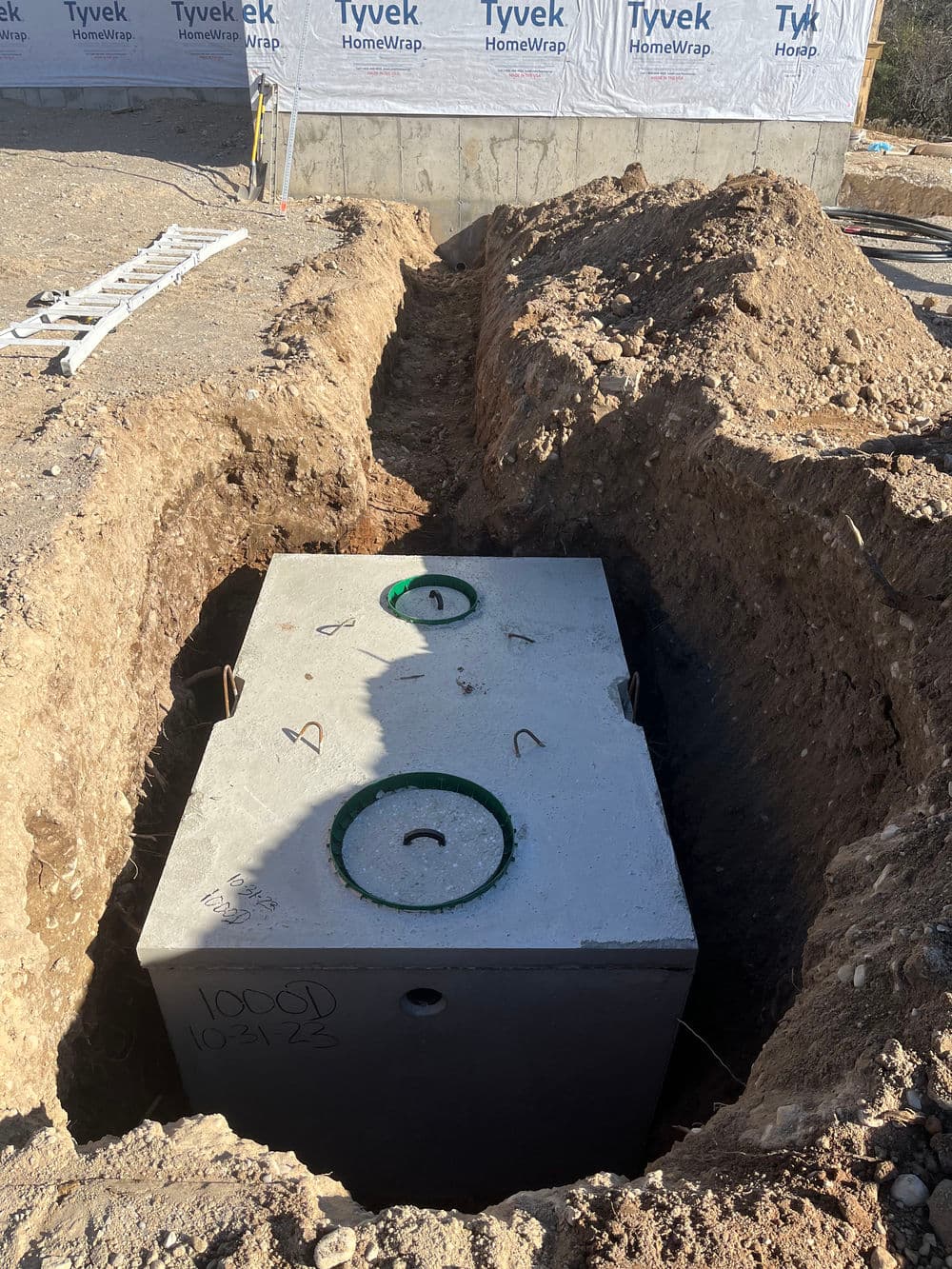 Concrete septic tank installation in a trench at a construction site.